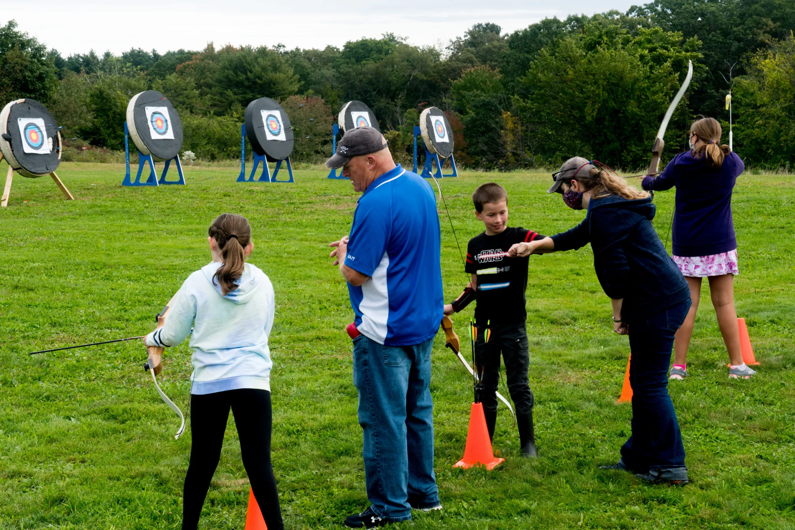Adult woman drawing a recurve bow at full draw, aiming at a target in an outdoor green field
