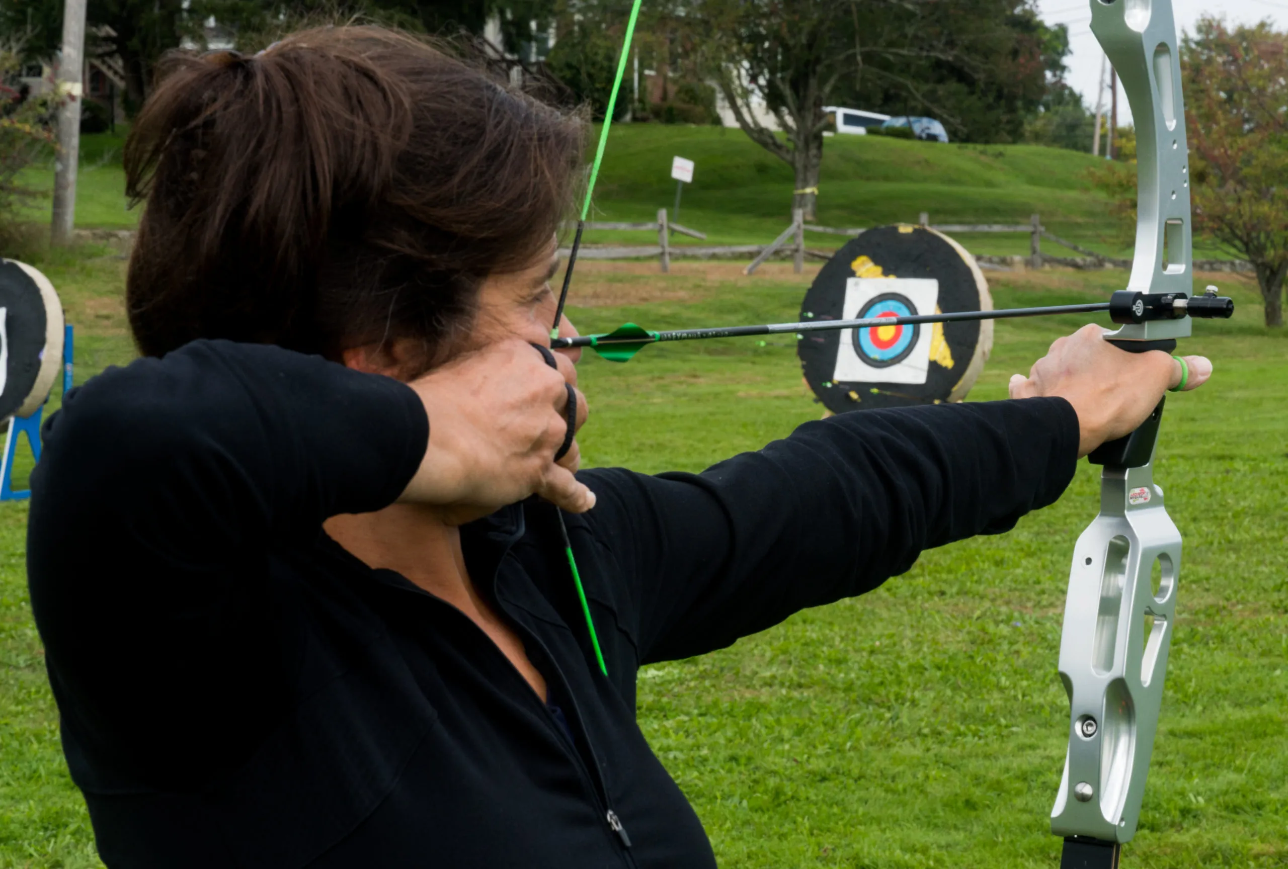 Young archers aiming bows at an outdoor archery tournament with orange cones marking shooting positions